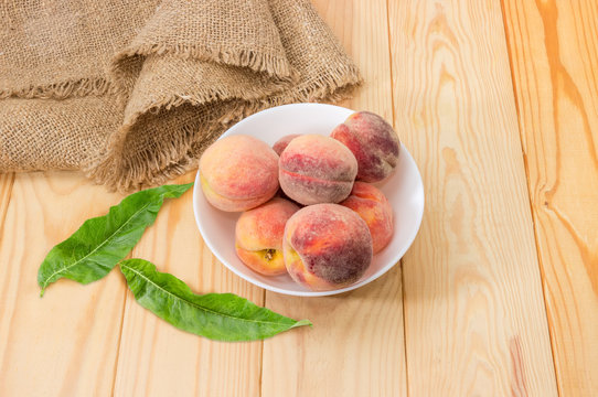 Fresh peaches in bowl and leaves on a wooden surface