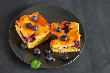 Two pieces of blueberry cake on a dark saucer.