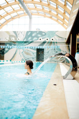 Young woman enjoying water splashes on her back while standing in spa swimming-pool