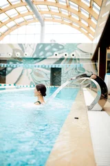 Gordijnen Young woman enjoying water splashes on her back while standing in spa swimming-pool © pressmaster