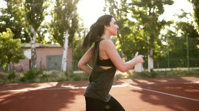 Fit woman in black sport bra and shirt running outdoors. Brunette girl with pony tail happilly jogging. Sunlight