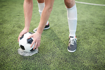 Young footballer putting soccer ball on special area on gren field before game