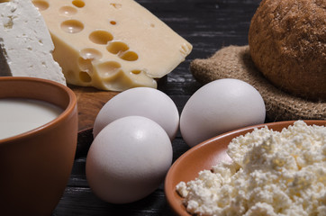 Rural breakfast. Bread, cheese, feta, cottage cheese, milk and eggs on a wooden black table.