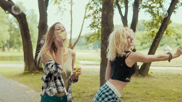 Happy hipster girls with sunglasses having fun making bubbles in park in slow motion