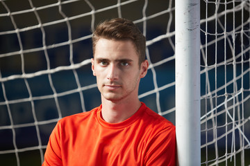 Young serious football player standing by net in front of camera on stadium