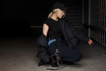 Stylish young model girl in a fashionable black winter jacket with a cap in fashionable pants with...