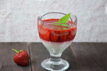 Summer dessert, panna cotta or yogurt or pudding or jam with strawberrieswith strawberries decorated with mint leaves. On a brown wooden table, bright sunlight. Copy space. close up