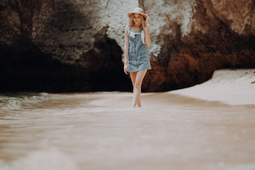 Young Woman walking on the beach in summer vacation wearing straw hat and beach dress enjoying the view at the ocean