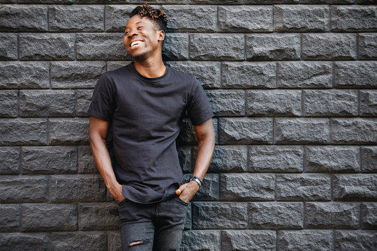 Handsome african american man in black t-shirt laughing against brick wall