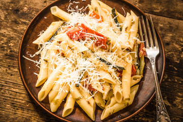 Classic Italian pasta with zucchini and tomatoes in a clay plate on a rustic table - top view