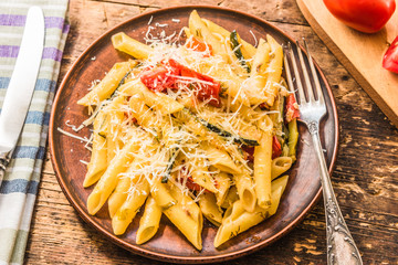 Classic Italian pasta with zucchini and tomatoes in a clay plate on a rustic table - top view
