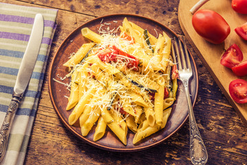 Classic Italian pasta with zucchini and tomatoes in a clay plate on a rustic table - top view