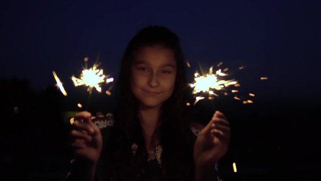 A young girl with long dark hair holds fireworks at night on the background of the city and rejoices. slow motion. HD.