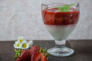 Summer dessert, panna cotta or yogurt or pudding or jam with strawberrieswith strawberries decorated with mint leaves. On a brown wooden table, bright sunlight. Copy space. close up
