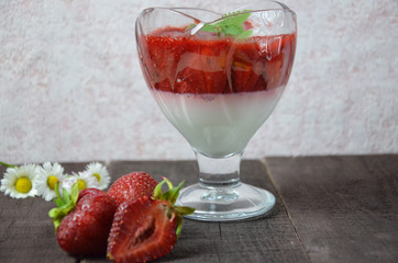 Summer dessert, panna cotta or yogurt or pudding or jam with strawberrieswith strawberries decorated with mint leaves. On a brown wooden table, bright sunlight. Copy space. close up