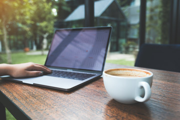 Fototapeta premium Closeup image of a woman working and typing on laptop keyboard with coffee cup on wooden table