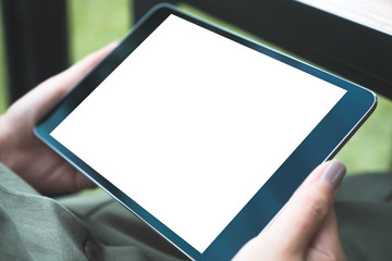 Mockup image of woman's hands holding black tablet pc with white blank screen while sitting in cafe with green nature background