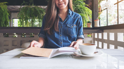 Closeup image of a woman opening a book with coffee cup on table in modern cafe