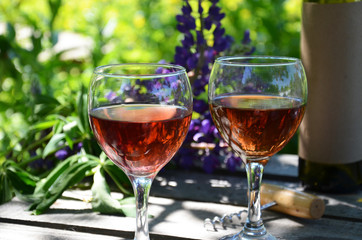 Red wine poured into wine glass on background of green tree leaf foliage. purple flower