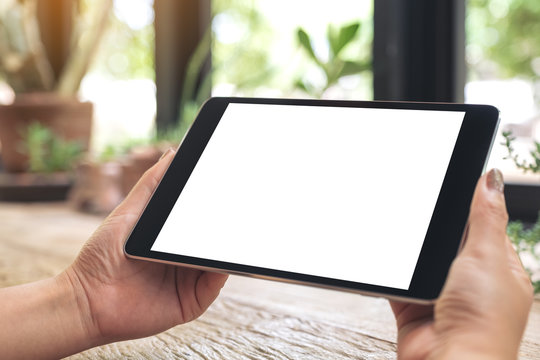 Mockup image of hands holding black tablet pc with blank white desktop screen on wooden table