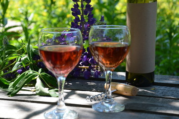 Red wine poured into wine glass on background of green tree leaf foliage. purple flower