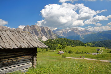 Fototapeta na wymiar Puez Odle mountain range (on the left) and Sella Group mountains (on the right) viewed from a hiking path near Raiser Pass with a mountain hut in the foreground, Val Gardena, Dolomites, Italy
