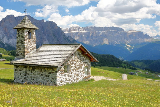 The Chapel of Mastle located near Raiser Pass, with Puez Odle mountain range and Sella Group mountains and with colorful flowers in the foreground, Val Gardena, Dolomites, Italy