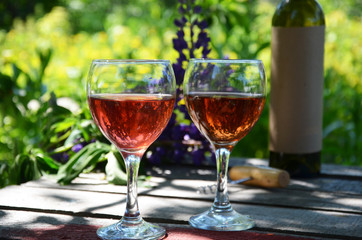 Red wine poured into wine glass on background of green tree leaf foliage. purple flower