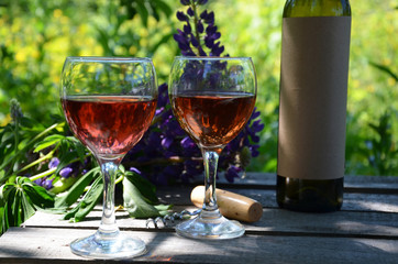 Red wine poured into wine glass on background of green tree leaf foliage. purple flower