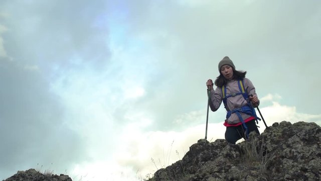 Back view of excited hipster girl standing on high mountain top feeling free raising hands up, happy female traveler with backpack celebrating achievement of reaching peak during hiking tour