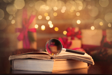magnifier and books on background with fairy lights and gifts in bokeh. Christmas Holiday season