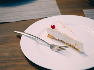 Piece of white chessecake with berry at plate in cafe