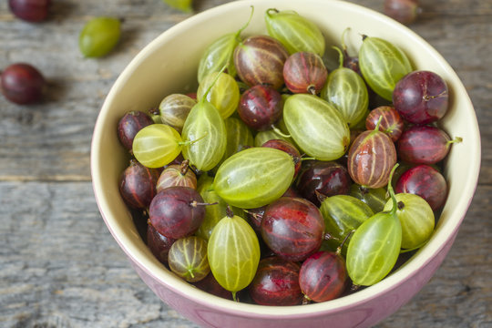 Gooseberry berries are red and white in a plate on a wooden rustic background.