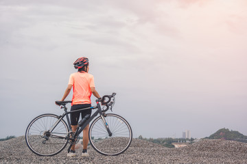 Young slim lady standing on top of a mountain with bicycle and enjoying valley view