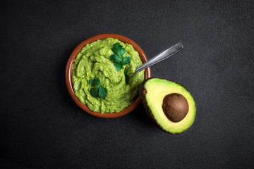 Traditional Mexican Dip Sauce Guacamole in a bowl with cutted in a  half avocado  on black background. Top view