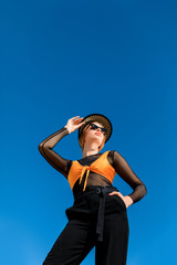 bottom view of girl posing in trendy sunglasses and stylish hat, blue sky on background