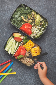 Healthy meal prep containers with quinoa, avocado, corn, zucchini noodles and kale. Child is eating at school from lunch box.