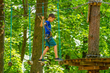 Naklejka na ściany i meble Boy kid enjoying activity in a climbing adventure park on a summer day