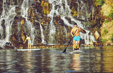positive smiling boy in rashguard and his young father enjoying stand up paddleboarding