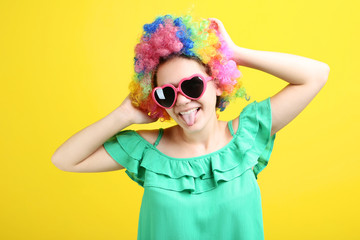 Young girl in clown wig and sunglasses on yellow background