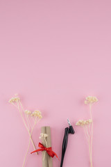 Scroll and oblique pen decorate with white dried flowers on pastel pink background with copy space 