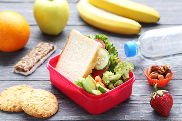 School lunch box with sandwich and vegetables on wooden table