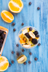 Top view of a cup full of tasty fruits in a cup . Berry, banana orange on wooden table