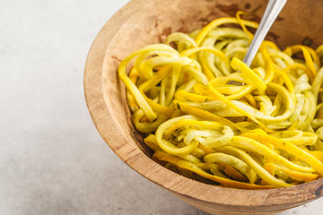 Raw vegan zucchini noodles in a wooden bowl, white background.