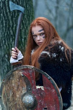 Portrait of female viking warrior woman holding ax and shield outdoor