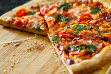 sliced Pizza with Mozzarella cheese, Ham, Tomatoes, pepper, Spices and Fresh Basil pesto sauce. Italian pizza.