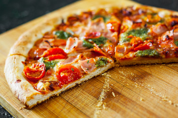 sliced Pizza with Mozzarella cheese, Ham, Tomatoes, pepper, Spices and Fresh Basil pesto sauce. Italian pizza.