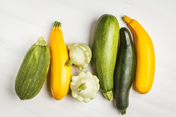 Different kinds of zucchini on white background, top view, copy space. Healthy clean eating concept.