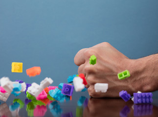 Hand hits to pile of colored toy bricks falling on blue background. Studio shooting. High speed freezing photo