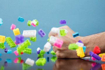 Hand hits to pile of colored toy bricks falling on blue background. Studio shooting. High speed freezing photo